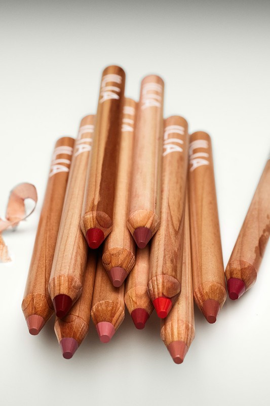 Close-up of wooden lip pencils with different shades of color, arranged on a white surface with subtle lighting, beauty product.