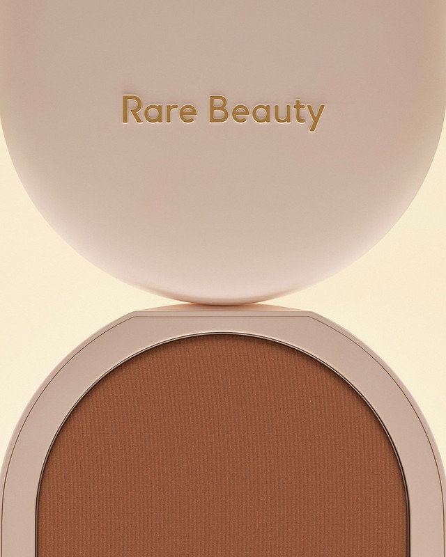 Close-up of a Rare Beauty bronzer compact showing the logo on the lid and the bronzer shade inside, creating a beauty product shot.