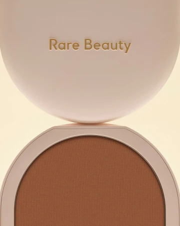 Close-up of a Rare Beauty bronzer compact showing the logo on the lid and the bronzer shade inside, creating a beauty product shot.