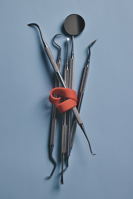 Dental tools bundled with orange rubber band on light blue background, showcasing instruments for dental healthcare.