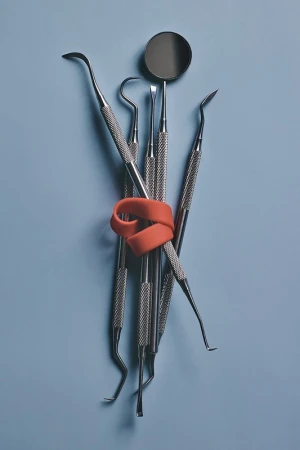 Dental tools bundled with orange rubber band on light blue background, showcasing instruments for dental healthcare.