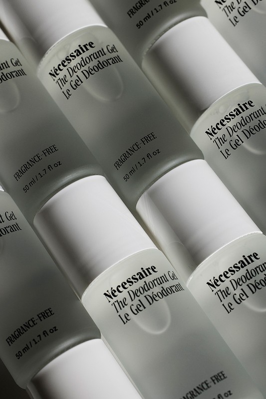 Close-up product shot of multiple frosted glass bottles of Nécessaire The Deodorant Gel with white caps aligned in a grid pattern.