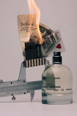 Perfume bottle with lit matches, playing card, money, and paper. Luxury and risk concept, product still life.