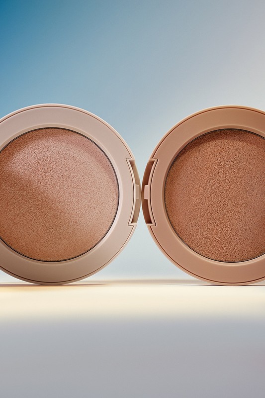 Two open compacts of bronzer makeup sit side-by-side, displaying warm brown powders against a pale blue background with neutral lighting.