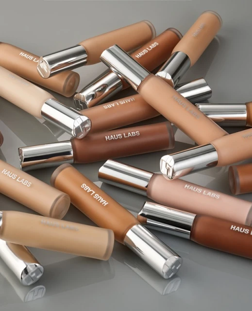Cosmetic product tubes of Haus Labs foundation in varying skin tones, arranged on a gray surface, showcasing a range of shades.