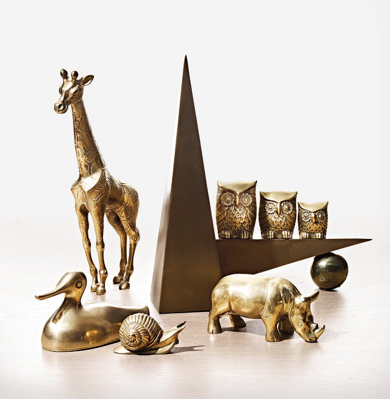Golden figurines of giraffe, rhino, owls, duck, snail, and geometric shapes on white background. Objects are arranged in a display.