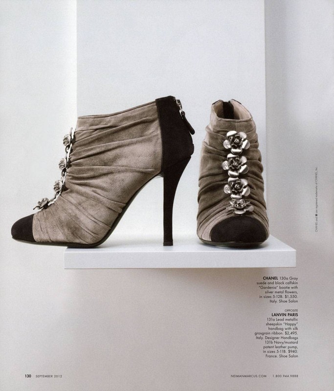 High-heeled ankle boots in gray suede with black accents, decorated with silver flowers, displayed on a white shelf in a magazine shot.