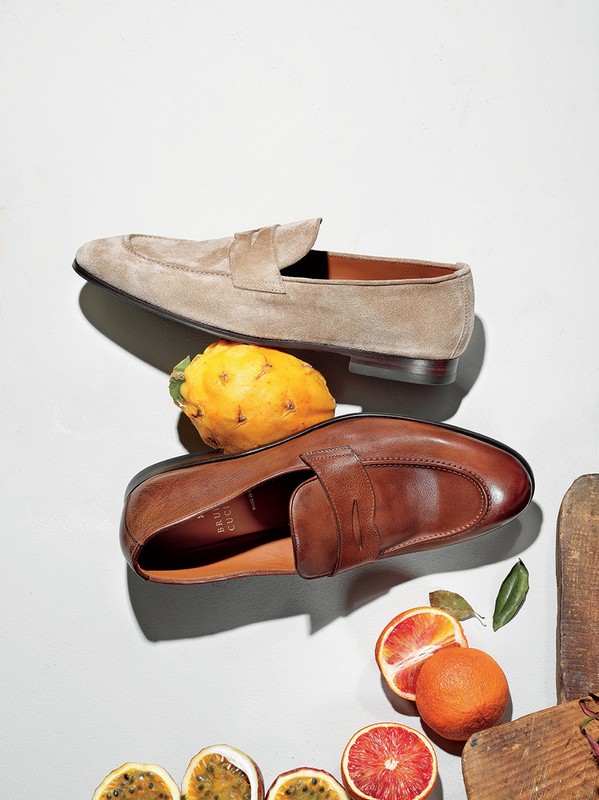 Close-up of brown and beige leather loafers arranged with citrus fruit, passionfruit, and dragonfruit on a white surface.