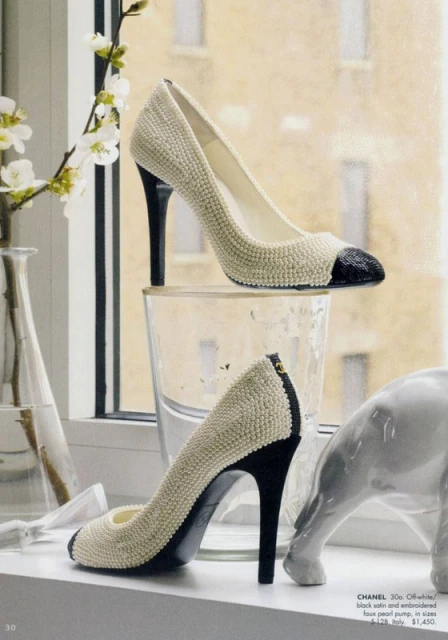 Elegant beige and black Chanel heels displayed on a window sill with a minimalist ceramic dog sculpture and white flowering branches.