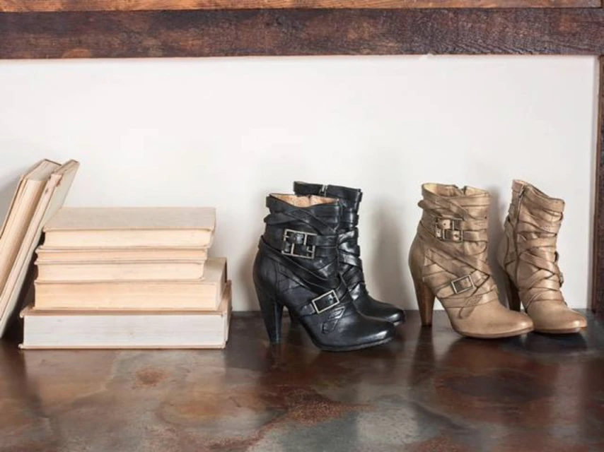 Two pairs of leather heeled ankle boots, one black and one tan, displayed on a marble surface with a stack of books in the background.