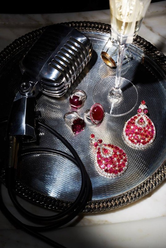 Close-up studio shot of a silver tray holding various jewelry, including rings and earrings, alongside a vintage microphone and champagne flute.