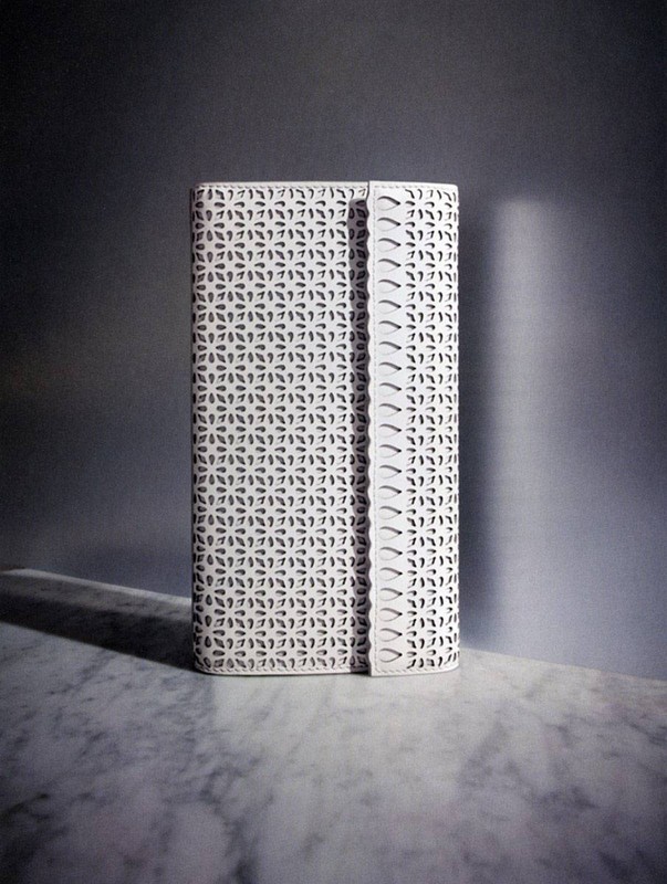 White patterned clutch on a marble surface in a studio with soft light creating a distinct shadow behind the accessory.