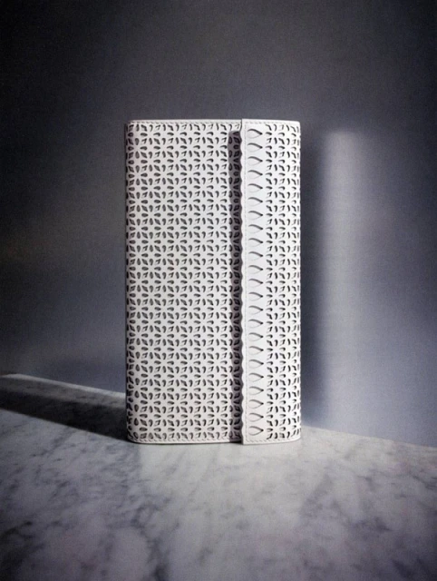 White patterned clutch on a marble surface in a studio with soft light creating a distinct shadow behind the accessory.