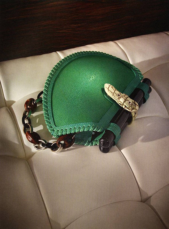 Green leather shoulder bag with dark tortoise chain handle and decorative snake detail resting on a white cushioned surface.