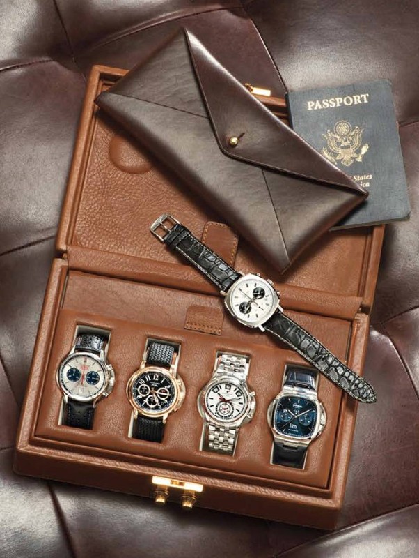 A collection of luxury watches presented in a brown leather box, accompanied by a passport and leather envelope on brown leather.