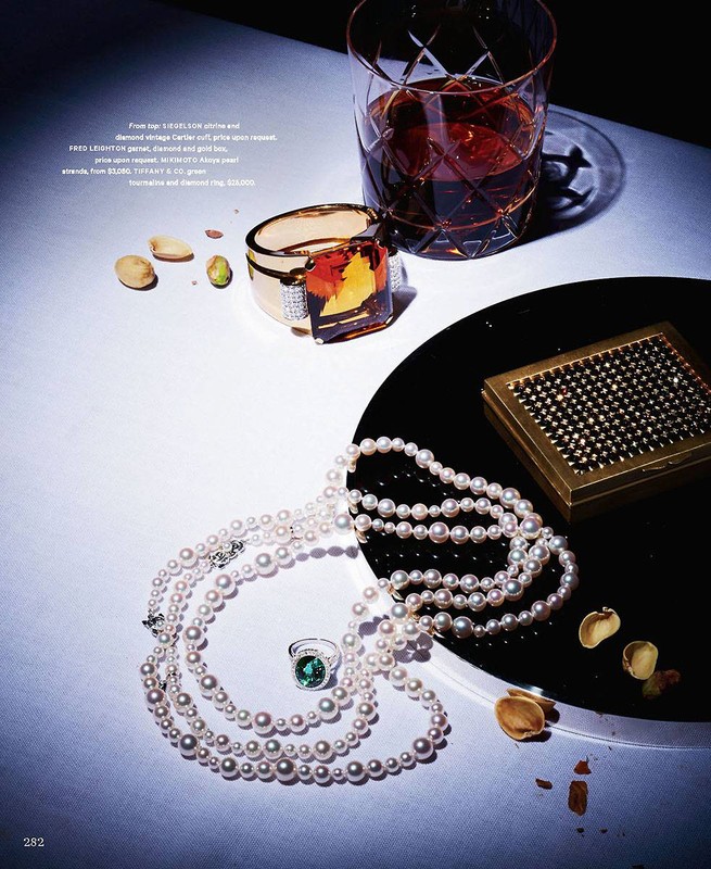 Elegant still life featuring pearl necklaces, a ring, a bracelet, a glass of liquor, and a gold box on a white and black surface.