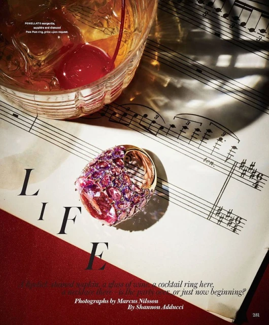 Cocktail ring with gemstones next to a cocktail with a cherry on sheet music for a vibrant editorial still life.