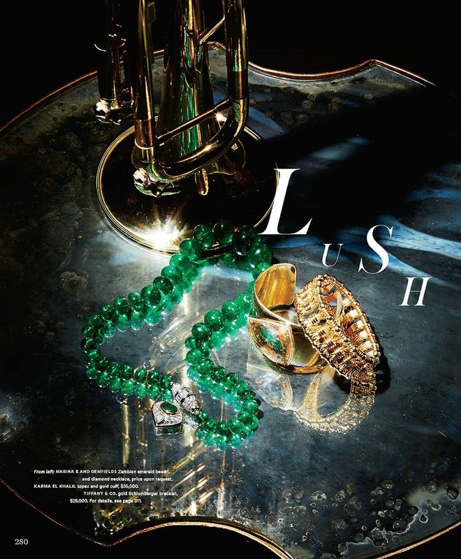 Still life featuring a gold-toned trumpet and emerald and gold jewelry on a reflective surface, showcasing luxury and musical elegance.