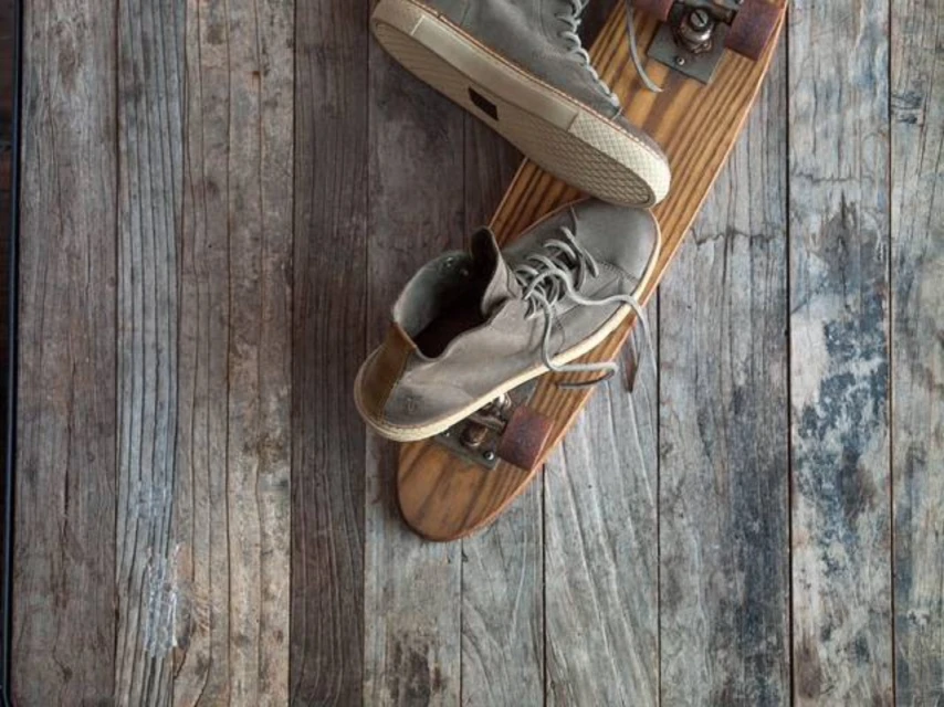 An eye-level, flat-lay photograph showcases worn grey shoes atop a skateboard, set against weathered wooden planks as a backdrop.