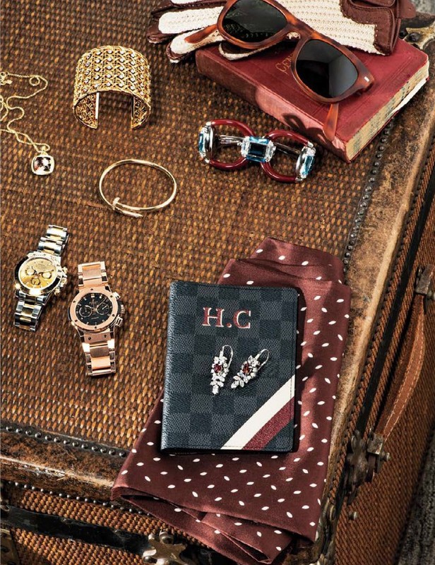 Close-up of a collection of accessories, including watches, jewelry, sunglasses, and a wallet, arranged on a textured surface.