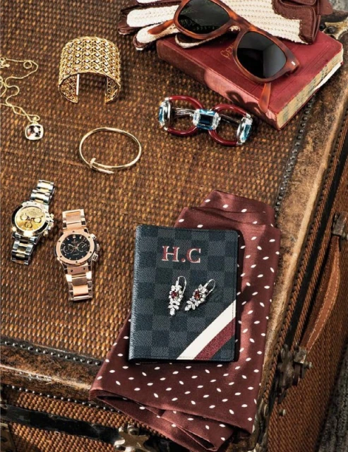 Close-up of a collection of accessories, including watches, jewelry, sunglasses, and a wallet, arranged on a textured surface.