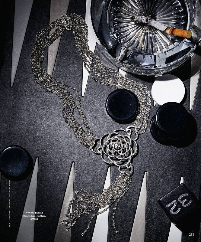 Overhead shot of Chanel diamond Camelia Brode necklace, backgammon pieces, cigarette in crystal ashtray, and black and silver board.