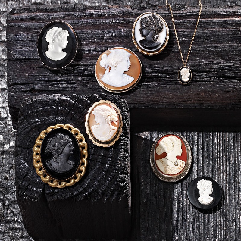 Arrangement of vintage cameo brooches and a necklace featuring carved figures, displayed on a dark, textured wooden surface.