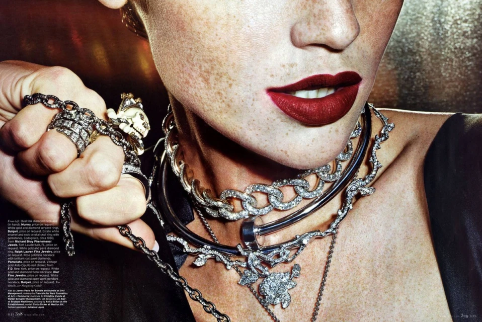 Close-up beauty shot of a fair-skinned adult female wearing dark red lipstick and statement jewelry, including rings and necklaces.