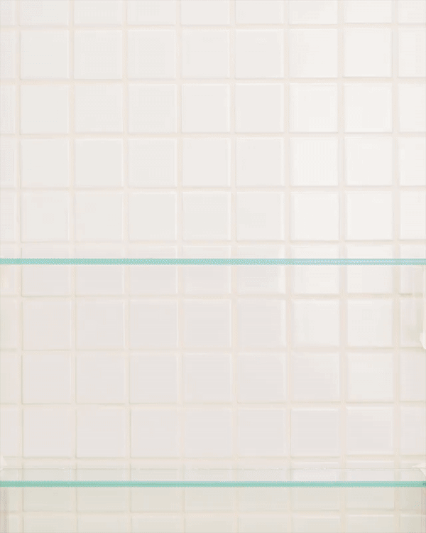 Close-up of a clean, white tiled wall with horizontal glass shelves in a minimalist design, creating a bright and airy aesthetic.