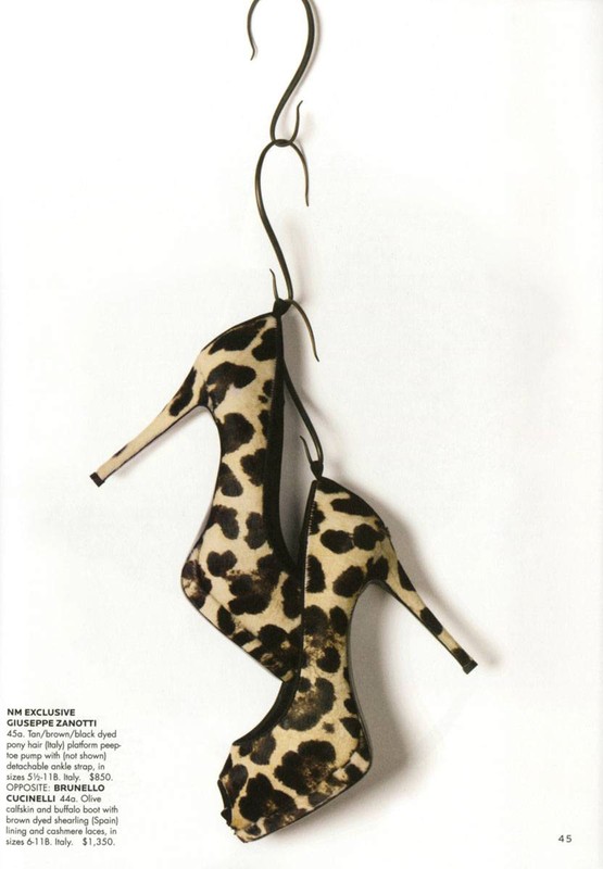 High heel shoes with black and tan animal print hanging from a dark metal s-hook against a plain white background.
