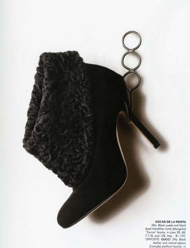 Black suede boot with Astrakhan lamb trim on a metal stand, featuring a pointed toe and stiletto heel against a white background.