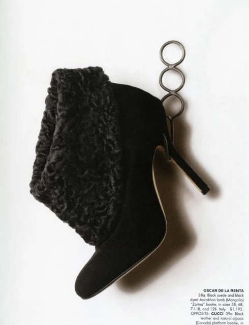 Black suede boot with Astrakhan lamb trim on a metal stand, featuring a pointed toe and stiletto heel against a white background.