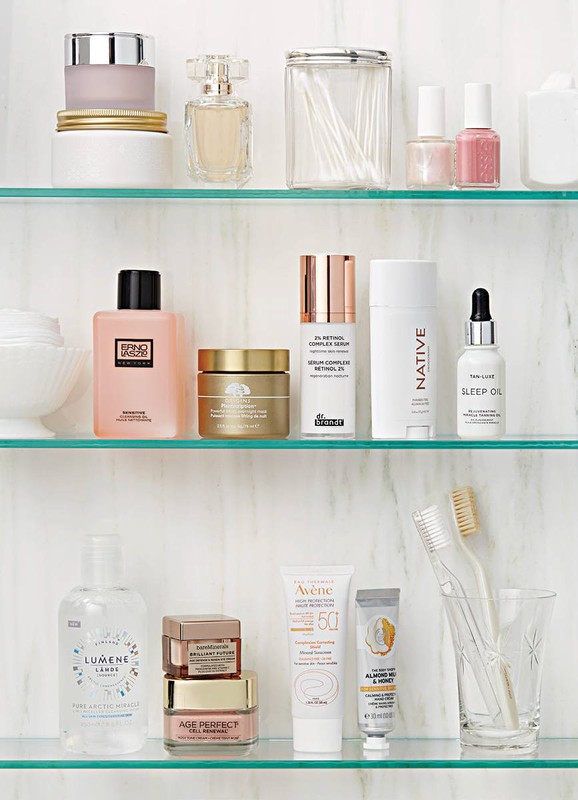 Assortment of skincare products including creams, lotions, and serums on clear glass shelves against a white marble background.