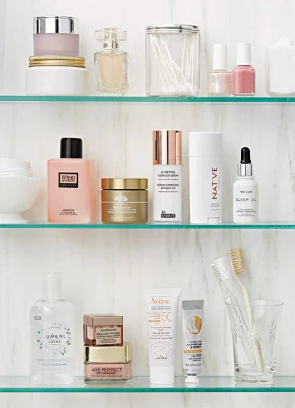 Assortment of skincare products including creams, lotions, and serums on clear glass shelves against a white marble background.