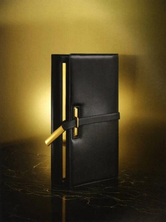 Studio shot of a black leather handbag with a gold accent on a marble surface against a gold background creating a high-fashion aesthetic.