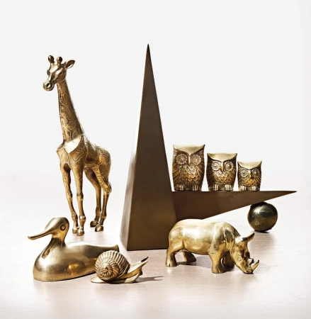 Arrangement of polished brass animal figurines including a tall giraffe, duck, snail, and rhinoceros against a plain white background.