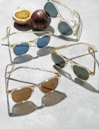 Four pairs of clear-framed sunglasses arranged on a textured grey surface alongside a whole and halved passionfruit.