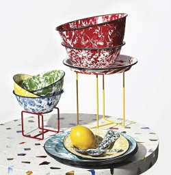 Stack of speckled red enamelware bowls and plates on metal stands with a lemon on a patterned table
