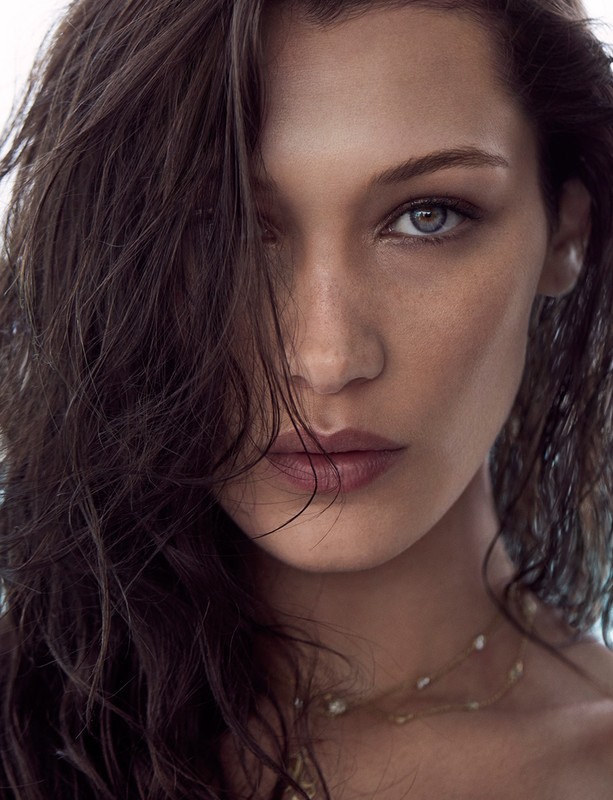 Close-up portrait of an adult woman with brown hair partially covering her face, gazing forward with light-colored eyes and wearing a delicate necklace.