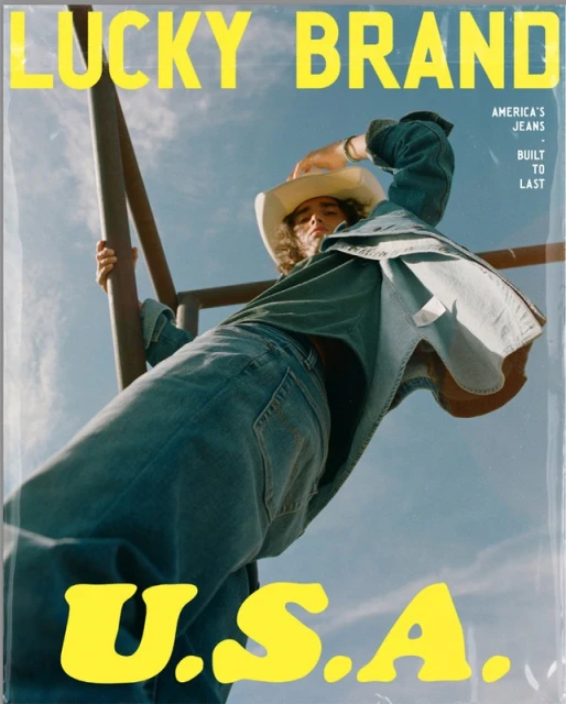A denim-clad person in a cowboy hat poses with weathered metal against a blue sky in a Lucky Brand advertisement with U.S.A. text.