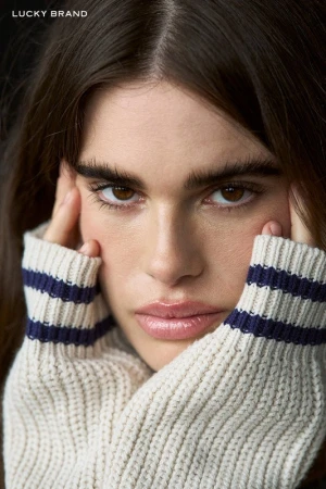 Close-up portrait of a woman wearing a cream sweater with navy stripes holding her face with her hands.