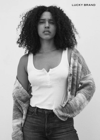 Black and white fashion portrait of a woman with curly hair wearing a white tank top and patterned cardigan.