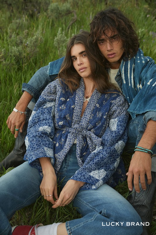 A young couple poses in an outdoor setting wearing denim clothing and jackets in a fashion editorial for Lucky Brand, captured at eye-level.