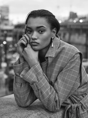 Black and white portrait of a woman resting chin on hands wearing a houndstooth coat against an outdoor city background
