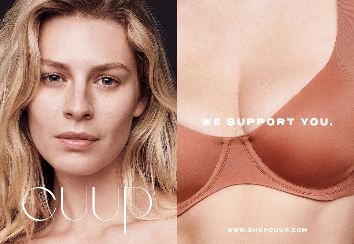 Close-up studio shot of a blonde adult female and a bra, with 'CUUP' and 'WE SUPPORT YOU' as text elements on a dark background.