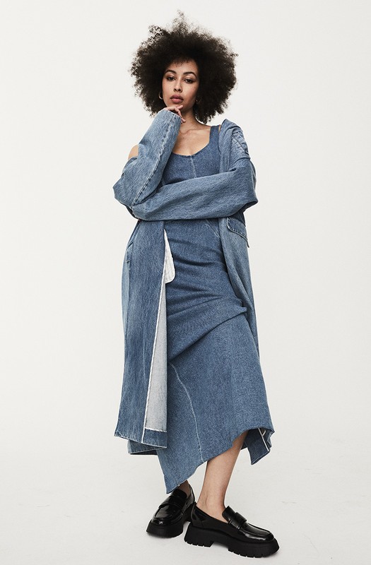 Full-length shot of a stylish adult woman with afro wearing a denim dress and jacket, standing in a photo studio, modern fashion.