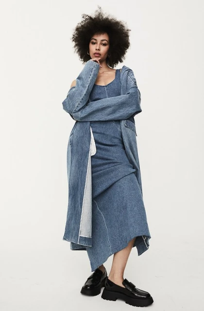 Full-length shot of a stylish adult woman with afro wearing a denim dress and jacket, standing in a photo studio, modern fashion.