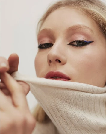 Close-up portrait of an adult woman with fair skin and blonde hair, showcasing makeup with pink eyeshadow and bold blue eyeliner.