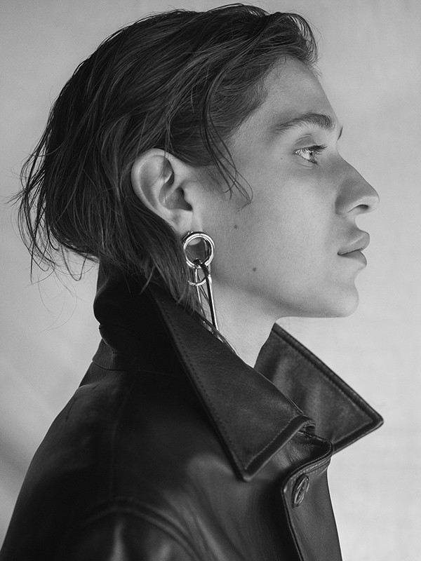 Monochrome portrait of a young adult male with dark hair wearing a black leather jacket and a silver earring in an indoor setting.