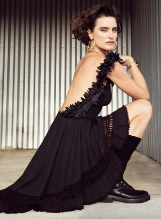 Woman in a black dress with ruffled trim and combat boots crouching against corrugated metal walls in Los Angeles.